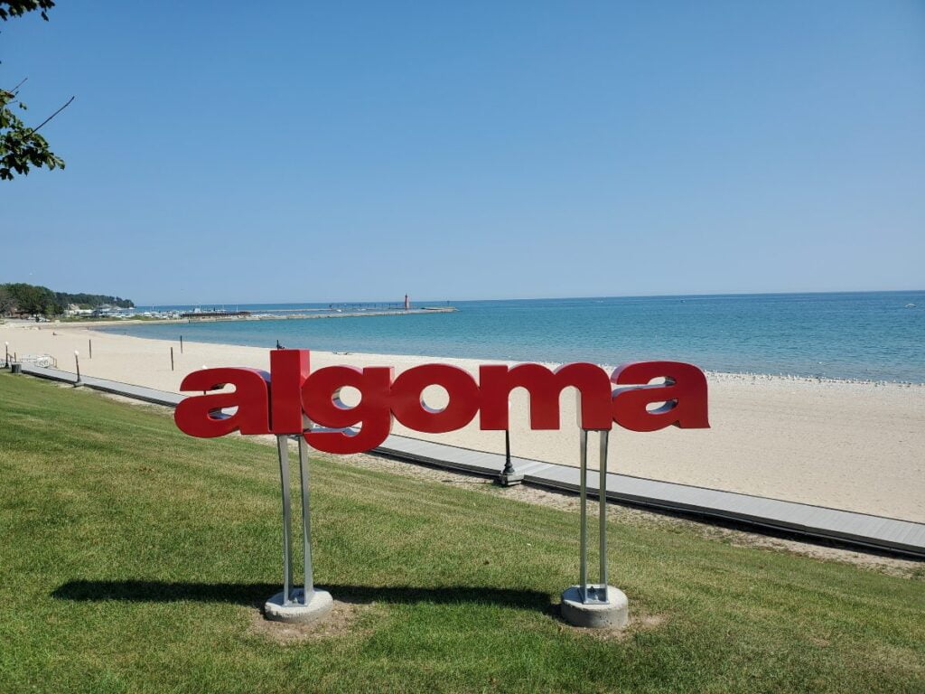 large red-lettered sign for Algoma, Wisconsin in front of a beach on Lake Michigan