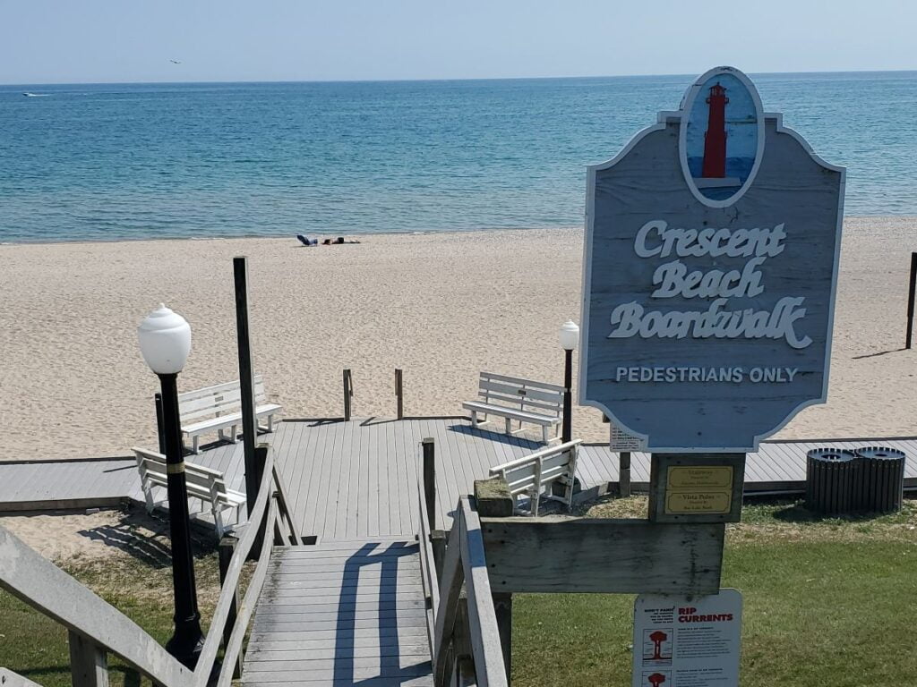 boardwalk along a sand beach in Algoma, WI with a sign that says "Crescent Beach Boardwalk"