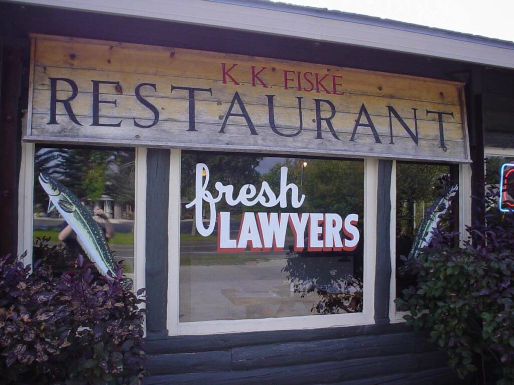 Signage on the outside of a restaurant that says: K.K. Fiske Restaurant. Fresh lawyers. Pictures of two lawyer fish.