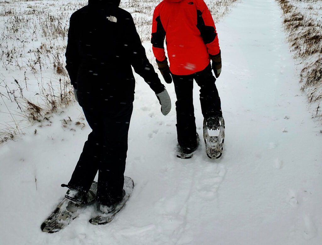 Two people walking in the snow with snowshoes.