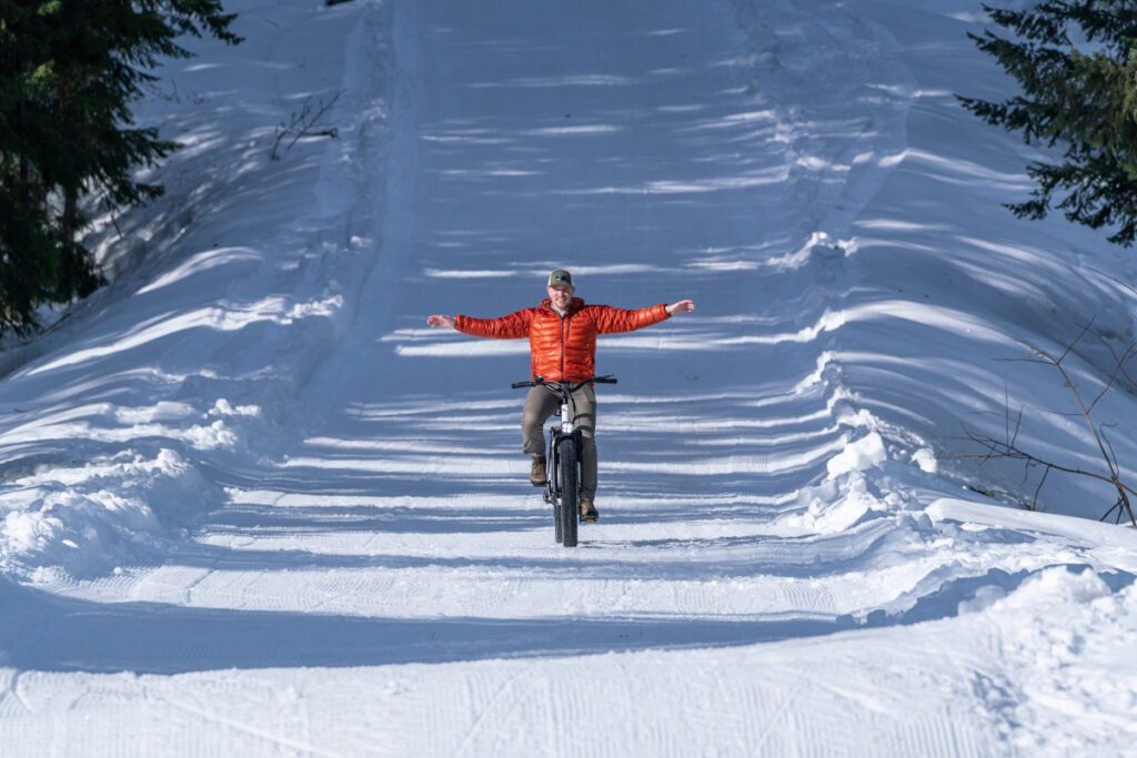 Man with arms outstretched on a fat tire bike in the snow.